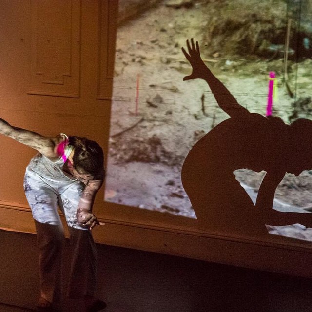 A dancer performs in front of a projected video. Its image projects onto her body.